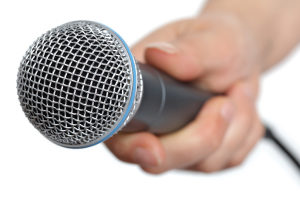 Interviewer holding a microphone, asking a job applicant if they have any questions for the interview panel